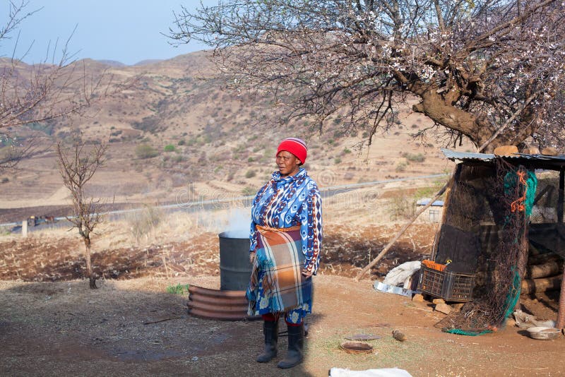 La mujer africana adulta en vestido combinado tradicional elabora cerveza la bebida nacional en barril del metal en el patio del fotos de archivo La mujer africana adulta en vestido combinado tradicional elabora cerveza la bebida nacional en barril del metal en el patio del fotos de archivo