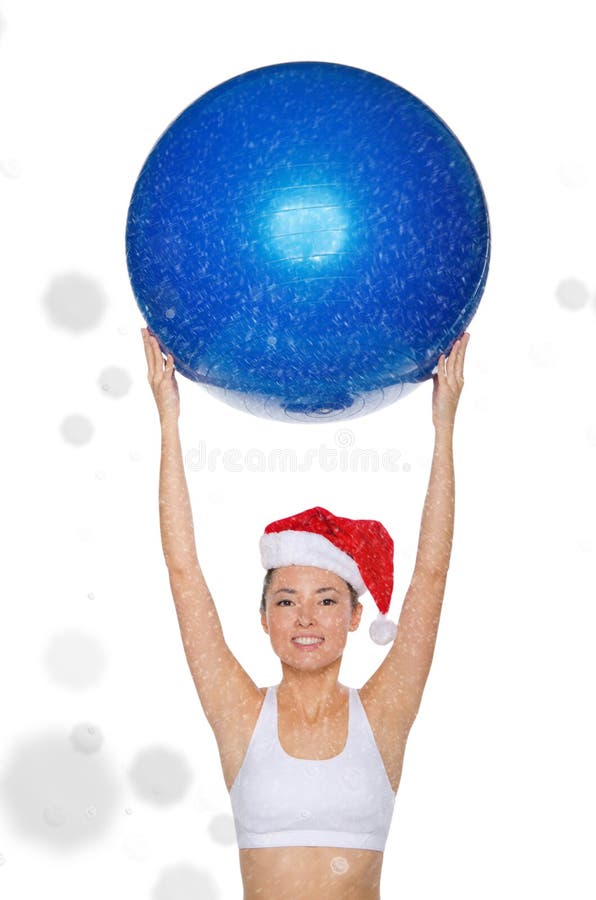 La mujer asiática sonriente en el casquillo de Papá Noel lleva a cabo el fitball debajo de nieve fotografía de archivo libre de regalías La mujer asiática sonriente en el casquillo de Papá Noel lleva a cabo el fitball debajo de nieve fotografía de archivo libre de regalías