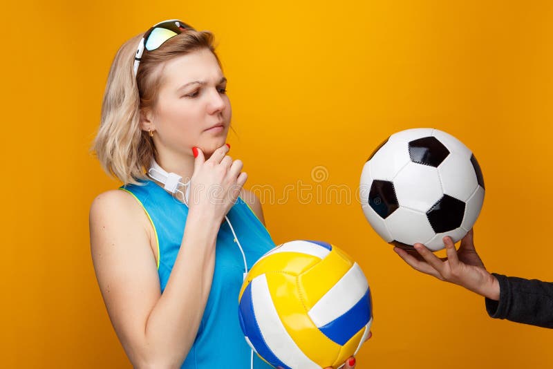 La mujer atlética elige entre el voleibol y el balón de fútbol en estudio fotografía de archivo La mujer atlética elige entre el voleibol y el balón de fútbol en estudio fotografía de archivo