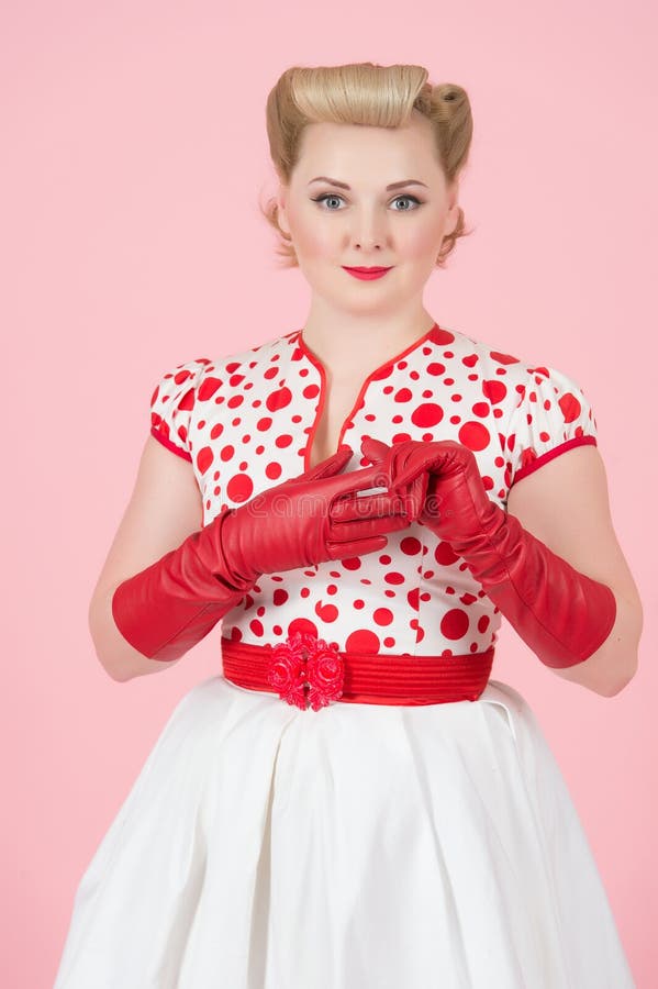 La mujer bonita diseñada perno-para arriba femenino rubio quita el guante rojo de la mano aislada en estudio con el fondo del ros imagenes de archivo La mujer bonita diseñada perno-para arriba femenino rubio quita el guante rojo de la mano aislada en estudio con el fondo del ros imagenes de archivo