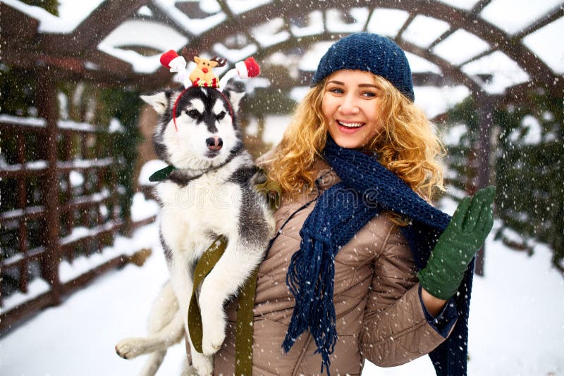 La mujer caucásica auténtica atractiva abraza el perro divertido del malamute que lleva las estimadas astas de la Navidad de sant fotos de archivo La mujer caucásica auténtica atractiva abraza el perro divertido del malamute que lleva las estimadas astas de la Navidad de sant fotos de archivo