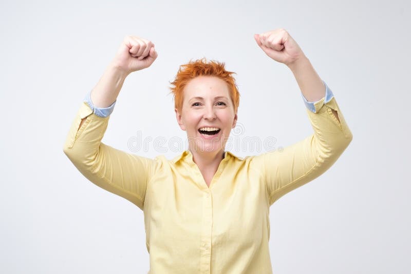 La mujer caucásica feliz con el pelo rojo exulta los puños de bombeo extáticos celebra éxito foto de archivo La mujer caucásica feliz con el pelo rojo exulta los puños de bombeo extáticos celebra éxito foto de archivo
