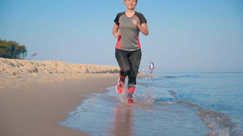 La mujer corre por la playa del mar