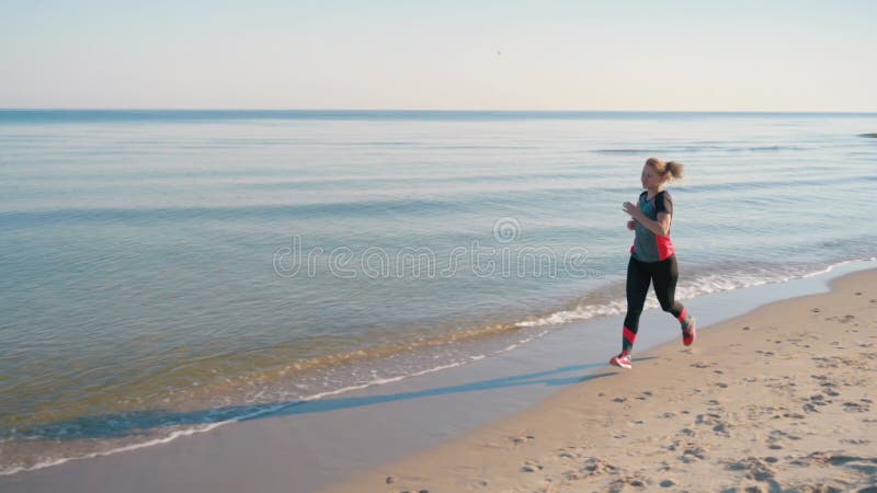 La mujer corre por la playa del mar