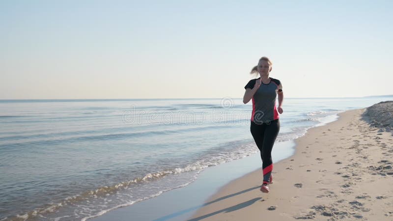 La mujer corre por la playa del mar