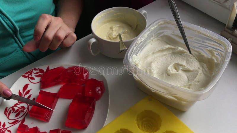 La mujer corta la jalea de la fresa Miente en un platillo blanco con un modelo rojo Cerca está un molde del silicón para hacer el