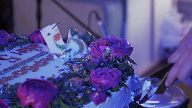 La mujer cortó la torta enorme con las rosas por dos cuchillos en el evento de la celebración Luz púrpura