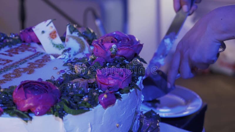 La mujer cortó la torta grande con las rosas por el cuchillo en el evento de la celebración Luz púrpura