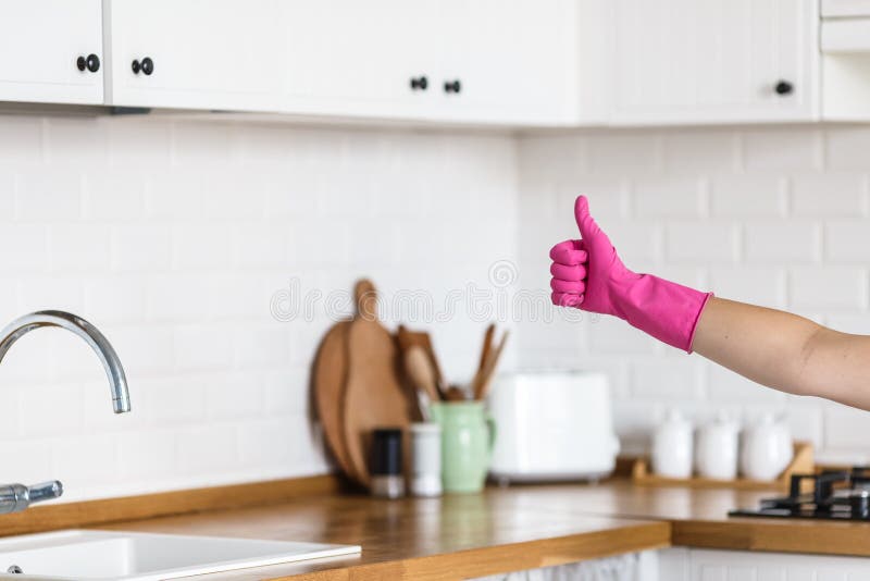 La mujer da guantes protectores que llevan en el fondo blanco de la cocina Concepto de cocina limpia, pulgar acertado para arriba imagen de archivo La mujer da guantes protectores que llevan en el fondo blanco de la cocina Concepto de cocina limpia, pulgar acertado para arriba imagen de archivo