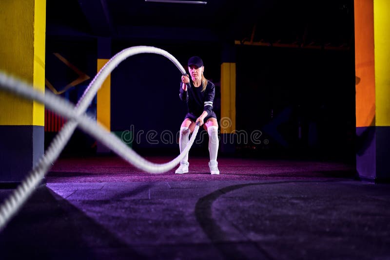 La mujer de la aptitud que usa el entrenamiento ropes para el ejercicio en el gimnasio El atleta que se resuelve con batalla rope fotos de archivo La mujer de la aptitud que usa el entrenamiento ropes para el ejercicio en el gimnasio El atleta que se resuelve con batalla rope fotos de archivo