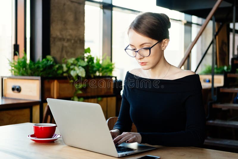 La mujer de negocios bonita joven trabaja en un ordenador portátil, aplicaciones un smartphone, freelancer, un ordenador, analist fotos de archivo La mujer de negocios bonita joven trabaja en un ordenador portátil, aplicaciones un smartphone, freelancer, un ordenador, analist fotos de archivo