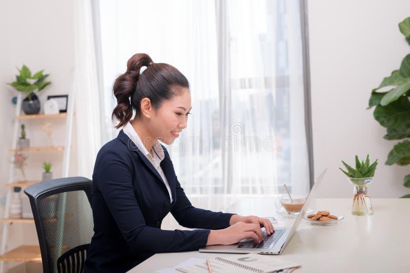 La mujer de negocios hermosa está utilizando un ordenador portátil y está sonriendo mientras que wor fotografía de archivo libre de regalías La mujer de negocios hermosa está utilizando un ordenador portátil y está sonriendo mientras que wor fotografía de archivo libre de regalías