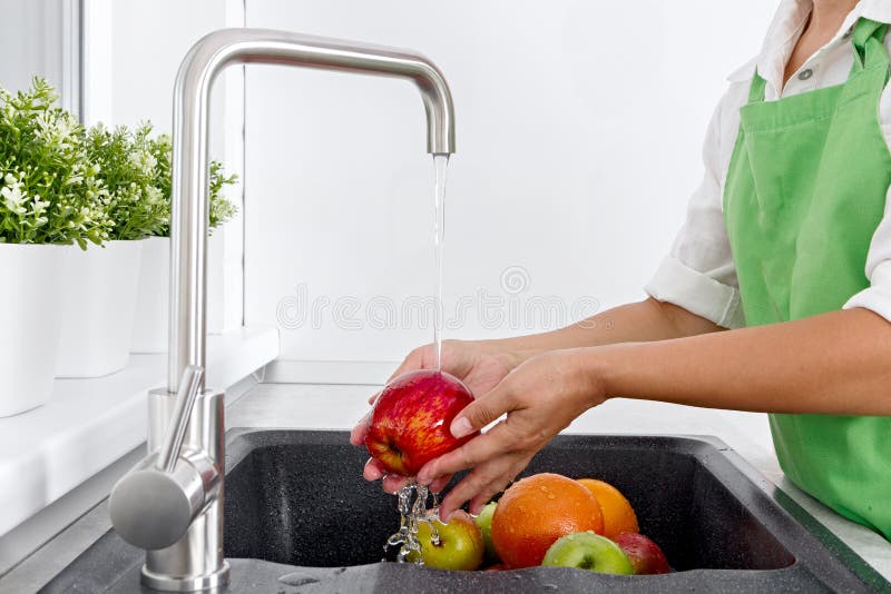La mujer del cocinero lava las frutas debajo de la agua corriente de un golpecito de agua imagen de archivo La mujer del cocinero lava las frutas debajo de la agua corriente de un golpecito de agua imagen de archivo