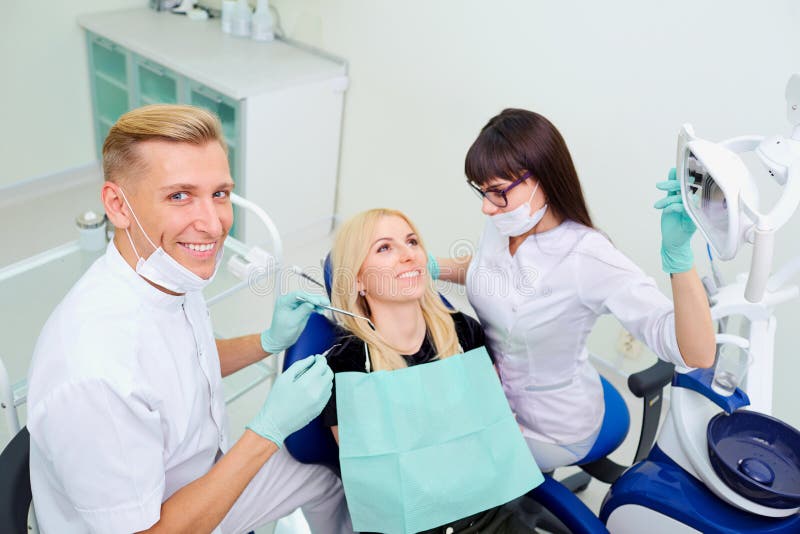 La mujer del hombre y del ayudante del dentista está tratando los dientes al cli imagen de archivo La mujer del hombre y del ayudante del dentista está tratando los dientes al cli imagen de archivo