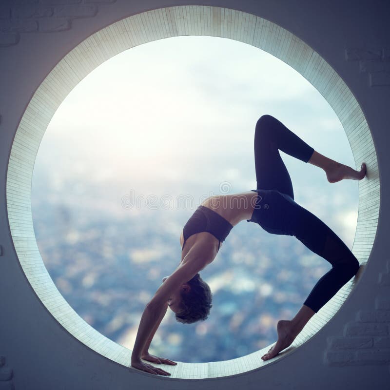 La mujer deportiva hermosa de la yogui del ajuste practica el asana Eka Pada Urdhva Dhanurasana de la yoga en una ventana redonda foto de archivo La mujer deportiva hermosa de la yogui del ajuste practica el asana Eka Pada Urdhva Dhanurasana de la yoga en una ventana redonda foto de archivo
