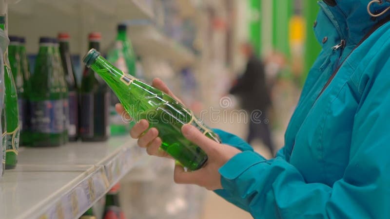 La mujer elige una botella de agua mineral en la tienda