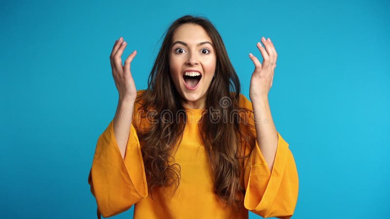 La mujer emocionada y sorprendida feliz disfruta de buenas noticias en fondo azul