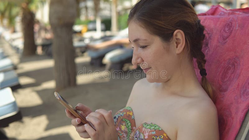 La mujer encantadora en traje de baño se sienta con smartphone foto de archivo libre de regalías La mujer encantadora en traje de baño se sienta con smartphone foto de archivo libre de regalías