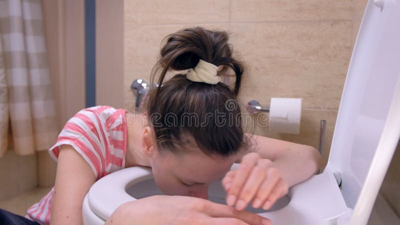 La mujer enferma joven está corriendo el retrete para vomitar sentarse en el piso, síntoma de la intoxicación alimentaria