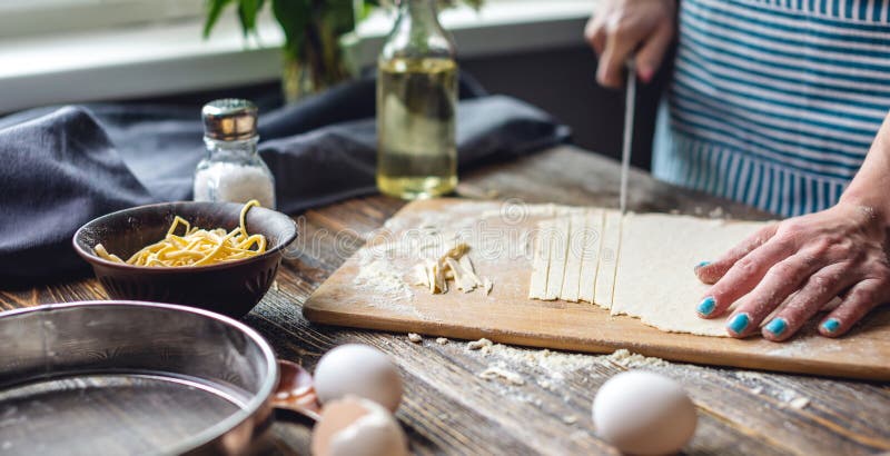 La mujer está cortando masa cruda con un cuchillo para hacer fideos caseros. concepto de proceso de cocción de pasta hecha a mano fotografía de archivo