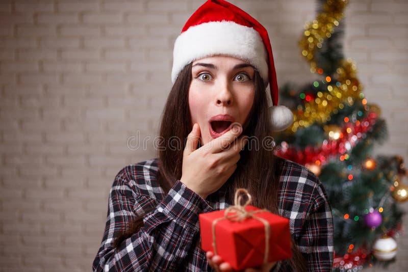 La mujer extremadamente sorprendida linda joven en el casquillo de Papá Noel es feliz a la GE imagen de archivo libre de regalías La mujer extremadamente sorprendida linda joven en el casquillo de Papá Noel es feliz a la GE imagen de archivo libre de regalías