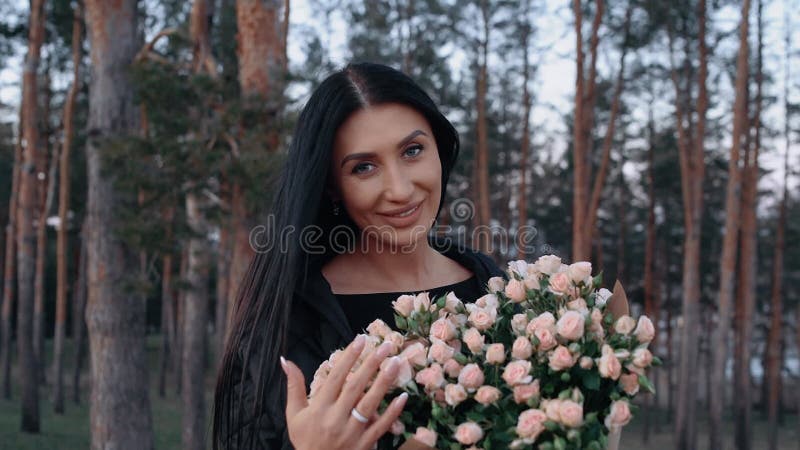 La mujer feliz huele el ramo de rosas blancas en el seno de la naturaleza en el prado verde cerca de la mesa para el