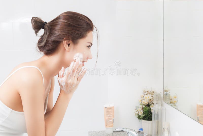 Woman happy cleanses the skin with foam in bathroom. Woman happy cleanses the skin with foam in bathroom