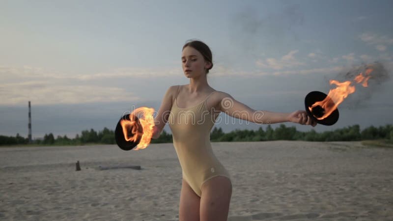 La mujer hermosa joven está bailando con el traje del cuerpo del fuego que lleva en salida del sol en el desierto