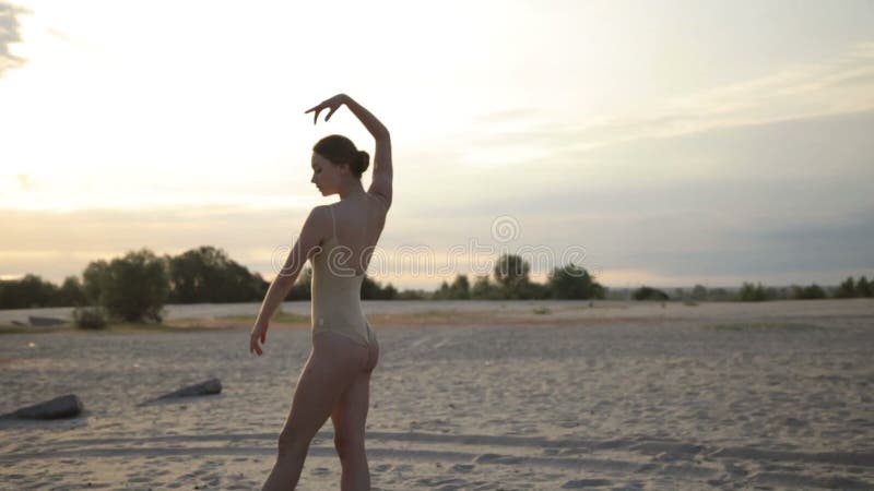 La mujer hermosa joven está bailando el traje del cuerpo que lleva en salida del sol en el desierto