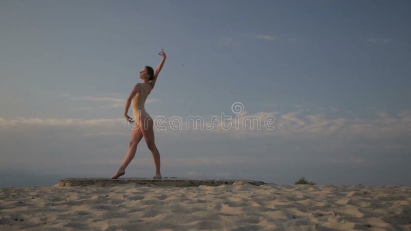 La mujer hermosa joven está bailando el traje del cuerpo que lleva en salida del sol en el desierto