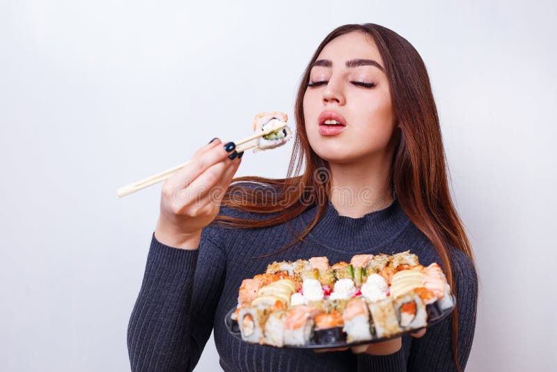 La mujer hermosa joven goza el comer del sushi, lanzamiento del estudio en blanco imagenes de archivo La mujer hermosa joven goza el comer del sushi, lanzamiento del estudio en blanco imagenes de archivo