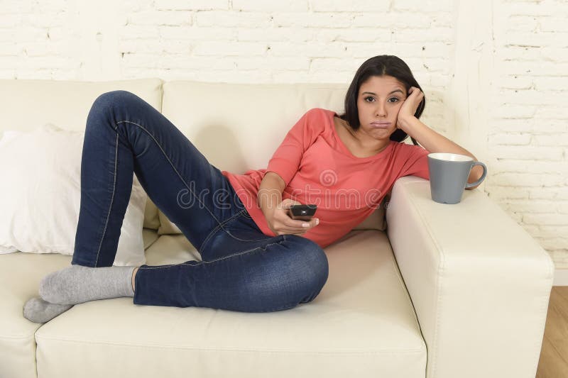 La mujer hispánica hermosa joven en casa que miraba la televisión cansó y agujereó fotografía de archivo La mujer hispánica hermosa joven en casa que miraba la televisión cansó y agujereó fotografía de archivo
