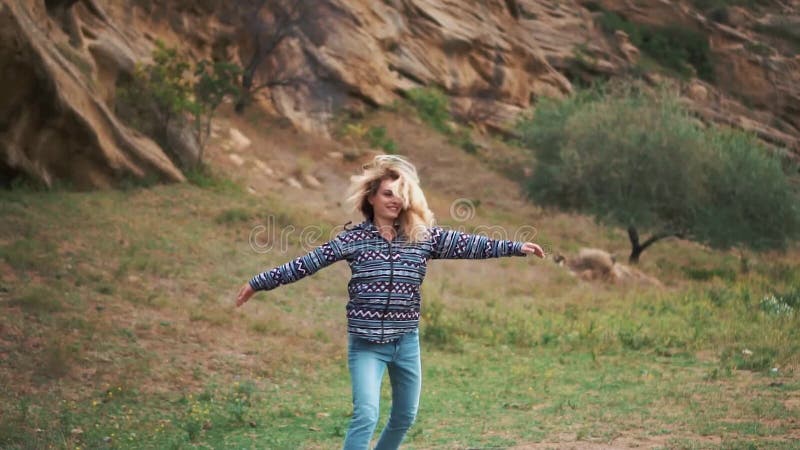 La mujer joven alegre con el pelo rubio en ropa azul floja del inconformista y gira feliz alrededor de sí misma en los años de