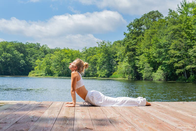 La mujer joven atractiva está practicando la yoga, haciendo actitud de la cobra cerca del lago fotos de archivo libres de regalías La mujer joven atractiva está practicando la yoga, haciendo actitud de la cobra cerca del lago fotos de archivo libres de regalías
