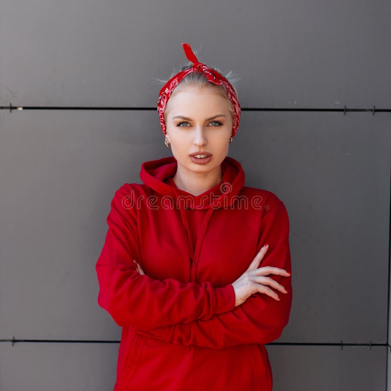 La mujer joven bonita elegante en ropa de moda moderna con un pañuelo rojo se está colocando cerca de un edificio moderno gris imagen de archivo libre de regalías La mujer joven bonita elegante en ropa de moda moderna con un pañuelo rojo se está colocando cerca de un edificio moderno gris imagen de archivo libre de regalías
