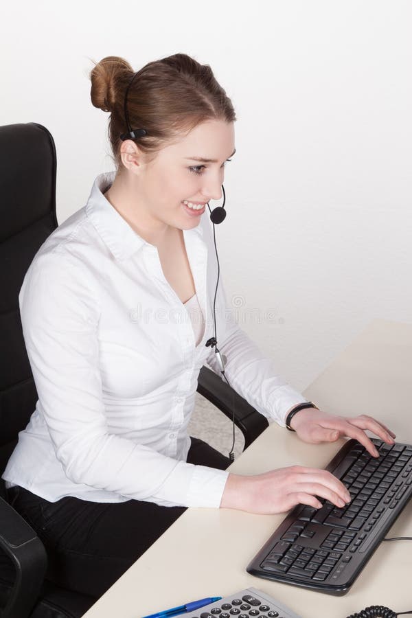 La mujer joven con las auriculares mecanografía en el teclado imágenes de archivo libres de regalías La mujer joven con las auriculares mecanografía en el teclado imágenes de archivo libres de regalías