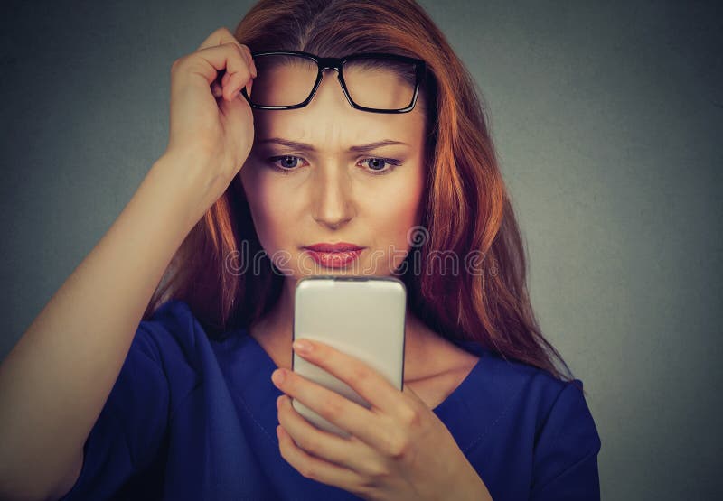 La mujer joven con los vidrios que tienen problema que ve el teléfono celular tiene problemas de la visión