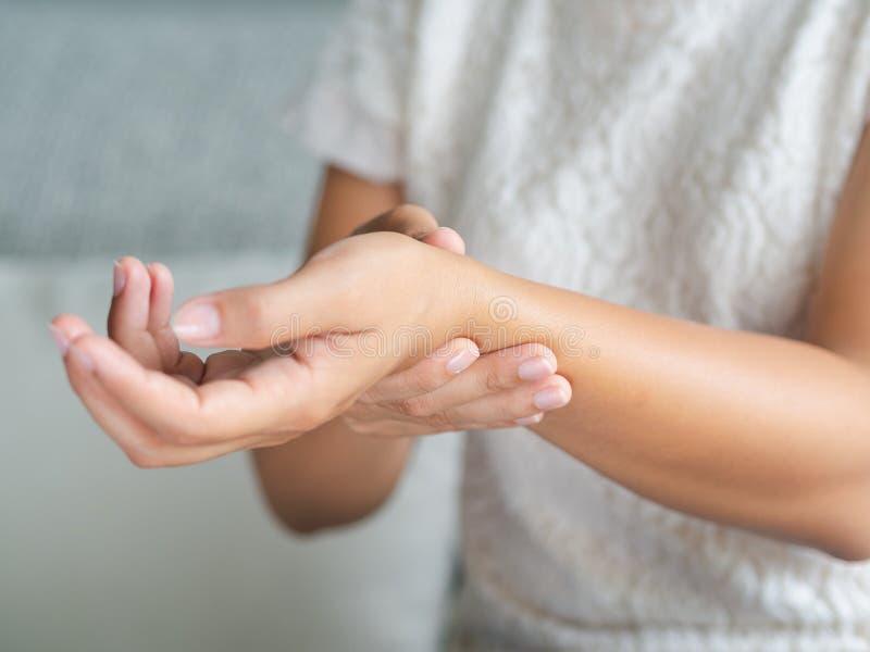 La mujer joven del primer que se sienta en el sofá lleva a cabo su lesión de mano de la muñeca foto de archivo La mujer joven del primer que se sienta en el sofá lleva a cabo su lesión de mano de la muñeca foto de archivo