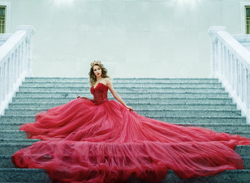 La mujer joven en un vestido rojo largo y el oro coronan sentarse en el st foto de archivo libre de regalías La mujer joven en un vestido rojo largo y el oro coronan sentarse en el st foto de archivo libre de regalías