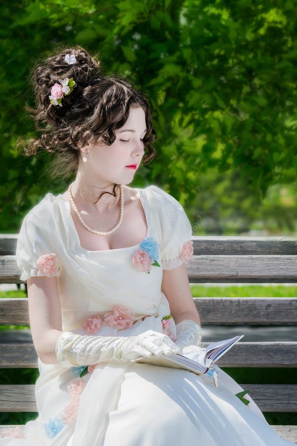 La mujer joven está leyendo un libro que se sienta en un banco fotografía de archivo La mujer joven está leyendo un libro que se sienta en un banco fotografía de archivo