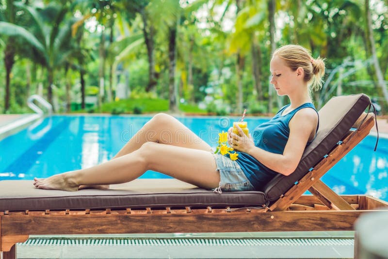 La mujer joven está sosteniendo un smoothie del mango en el fondo de la piscina Smoothie de la fruta - concepto sano de la consum foto de archivo La mujer joven está sosteniendo un smoothie del mango en el fondo de la piscina Smoothie de la fruta - concepto sano de la consum foto de archivo