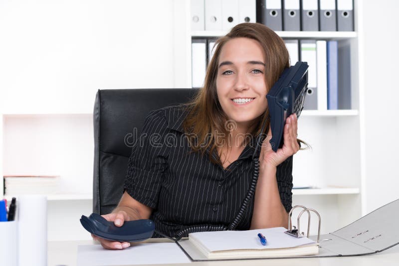 La mujer joven está sosteniendo un teléfono en su oído fotografía de archivo La mujer joven está sosteniendo un teléfono en su oído fotografía de archivo