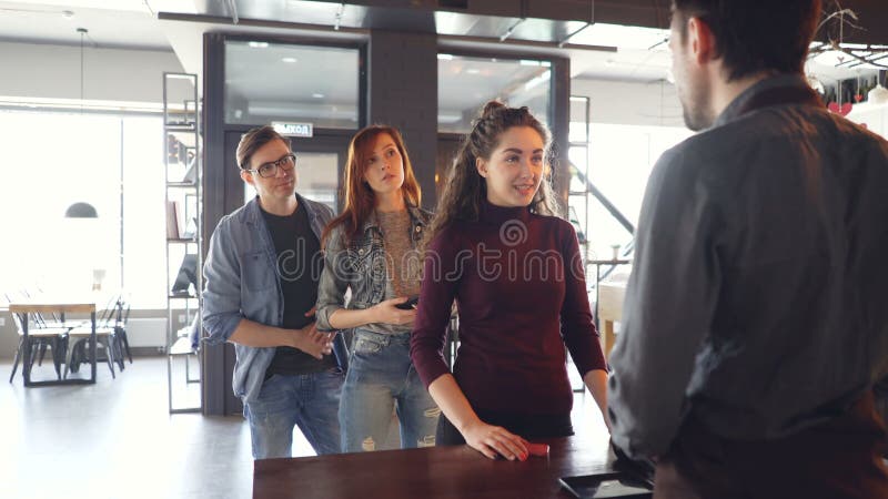 La mujer joven habladora está charlando con el cajero en el contador en café mientras que la gente impaciente se está colocando e