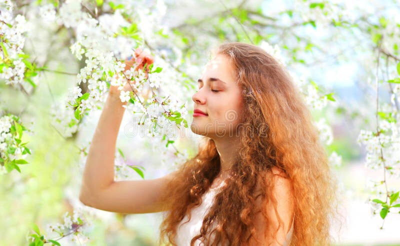 La mujer joven hermosa goza de las flores de la primavera del olor sobre jardín fotografía de archivo libre de regalías La mujer joven hermosa goza de las flores de la primavera del olor sobre jardín fotografía de archivo libre de regalías