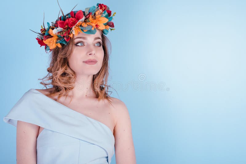 La mujer joven rubia hermosa con las flores enrruella, pelo rizado largo y maquillaje en fondo azul imagen de archivo La mujer joven rubia hermosa con las flores enrruella, pelo rizado largo y maquillaje en fondo azul imagen de archivo