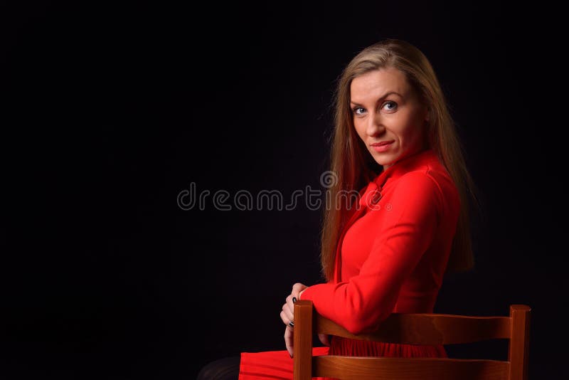 La mujer joven rubia hermosa en un vestido rojo se está sentando en un chai fotos de archivo libres de regalías La mujer joven rubia hermosa en un vestido rojo se está sentando en un chai fotos de archivo libres de regalías