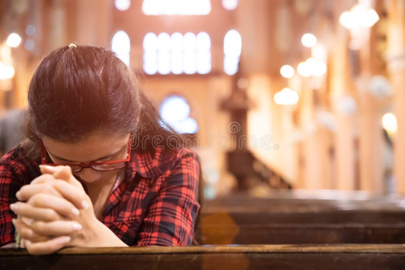 La mujer joven se sienta en un banco en la iglesia y ruega a dios Manos dobladas en el concepto del rezo para la fe imágenes de archivo libres de regalías