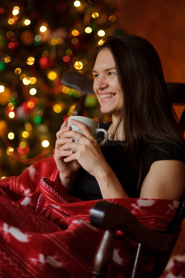 La mujer joven se sienta en una mecedora cerca del árbol de navidad fotografía de archivo La mujer joven se sienta en una mecedora cerca del árbol de navidad fotografía de archivo