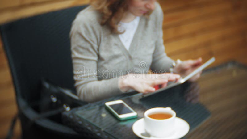 La mujer joven utiliza una tableta y el teléfono, bebe té en una barra del café almacen de video