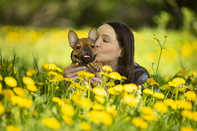 La mujer joven y un perrito del dogo francés están descansando en un parque imagenes de archivo La mujer joven y un perrito del dogo francés están descansando en un parque imagenes de archivo